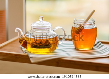 A transparent glass teapot with herbal tea and mint, next to a jar of honey.