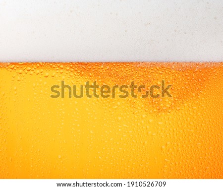 Close up background texture of pouring lager beer with bubbles and froth in frosty glass with drops, low angle side view Royalty-Free Stock Photo #1910526709