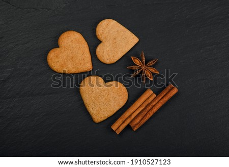 Close up heart shaped gingerbread cookies with cinnamon and star anise spices on black slate background with copy space, elevated top view, directly above