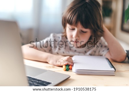 Distance learning online education. Caucasian smile kid boy studying at home with laptop and doing school homework. Thinking child siting at table with notebook. Back to school.