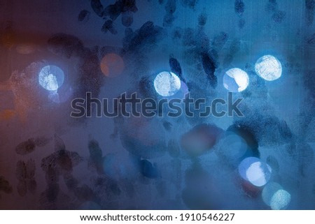 blue night wet window surface vith multiple palm prints on it