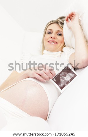 pregnant woman resting in bed with a sonogram of her baby