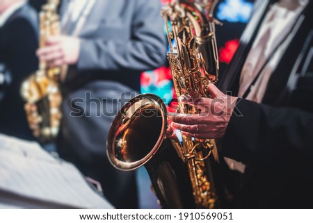 Concert view of a saxophonist, saxophone sax player with vocalist and musical during jazz orchestra performing music on stage  Royalty-Free Stock Photo #1910569051