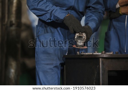 Young manual worker using grinder on metal in factory. Worker grinding in a workshop. Heavy industry factory, metalwork