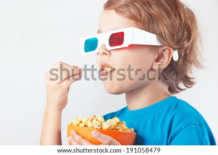 Young blonde boy in 3D glasses eating popcorn on white background