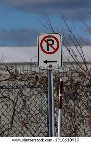a white metal sign with the words prohibiting parking stuck on a cedar hedge
