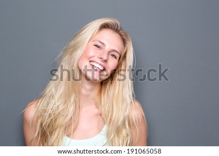 Close up portrait of a cheerful young blond woman smiling on gray background