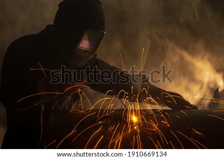 Industry welder working with electrode at arc welding in construction site.Welders working at the factory made metal parts in a protective suit. Royalty-Free Stock Photo #1910669134