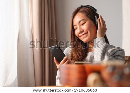 A beautiful young asian woman with headphone enjoy listening to music  on smart phone at home
