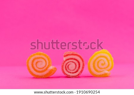 Closed up three spiral shape jelly candy, yellow red orange roll with sugar surface, pastel bright pink background