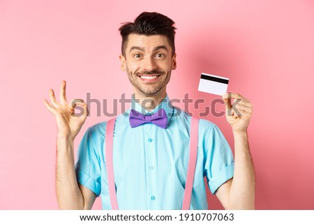 Shopping concept. Smiling handsome male shopper showing Ok sign and plastic credit card, buying something, standing satisfied on pink background