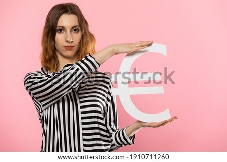 The girl holds a large euro symbol in her hands. Shape of the currency of the European Union. Symbol of finance and cash flow in the economy and the stock market on a solid background.