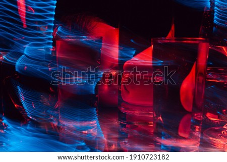 psychedelic strange portrait of a man looking through glasses of water with blur and red and blue neon lights