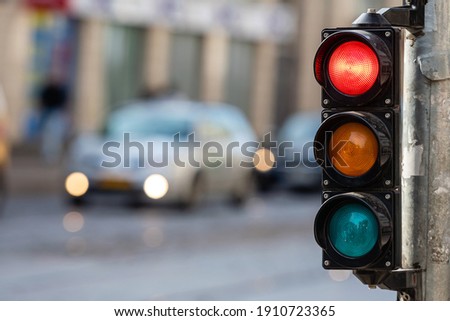 blurred view of city traffic with traffic lights, in the foreground a semaphore with a red light Royalty-Free Stock Photo #1910723365
