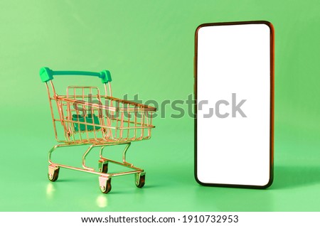 green metal cart and smartphone with white screen on green background, online shopping concept