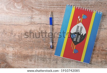 Notepad with Swaziland flag, pen on wooden background, study concept