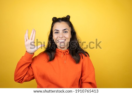 Young beautiful woman wearing sweatshirt over isolated yellow background doing hand symbol