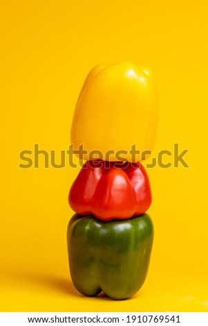Column of yellow, red and green colorful paprika vegetable peppers stacked on top of each other. Studio food still life contrasted against a seamless dark yellow background.