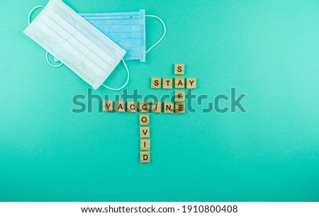 Words Covid Vaccine stay safe. The phrase is laid out in wooden letters. Top view. Motivation. Medical masks. Blue background. Mask. Copy space.