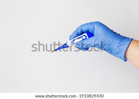 Human hand in a blue protective glove holding a white-blue thermometer in his hand on a white background.