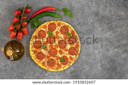 Tasty pepperoni pizza and cooking ingredients tomatoes, chili, basil on grey background. Top view, copy space.