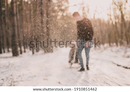 
A man rolls a woman on a sled in the forest with snow in focus