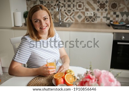 young woman in the kitchen drinks orange juice and smiles. healthy eating. bright kitchen Royalty-Free Stock Photo #1910856646