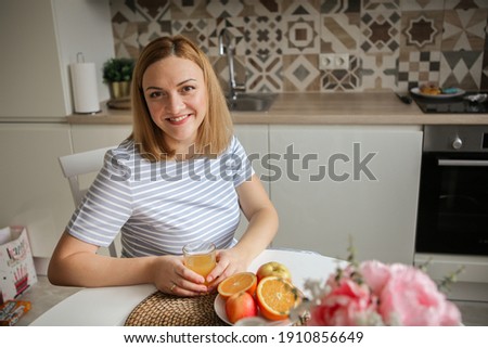 young woman in the kitchen drinks orange juice and smiles. healthy eating. bright kitchen Royalty-Free Stock Photo #1910856649