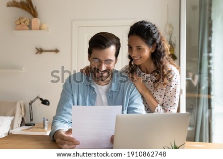 Happy young wife embrace shoulders of beloved husband reading official paper letter of getting job promotion loan mortgage approval. Glad married couple impressed with perfect news received by mail Royalty-Free Stock Photo #1910862748