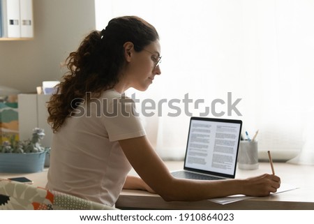 Confident female interpreter translate document from foreign language to english use pc app make notes in paper copy. Professional young woman editor correct errors mistakes in printed article text Royalty-Free Stock Photo #1910864023