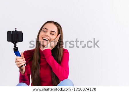 Caucasian brunette girl smiling holds a smartphone on a selfie stick and maintains her blog. White background with side space.