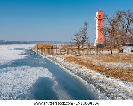 view to the river bank and red lighthouse behind trees under blue sky with copy space	
