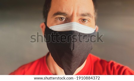 A white male wearing double protective masks against covid 19 looks at the camera against a seamless background