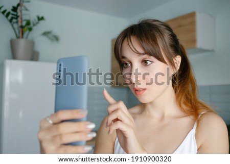 Young pretty girl with the bangs reading a message or shopping online in a smartphone at home in blue interior