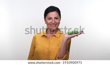 Cheerful old lady holding small green box in hand and pointing with her finger, isolated on white background. Creative people can put the product they want in the woman's hand.