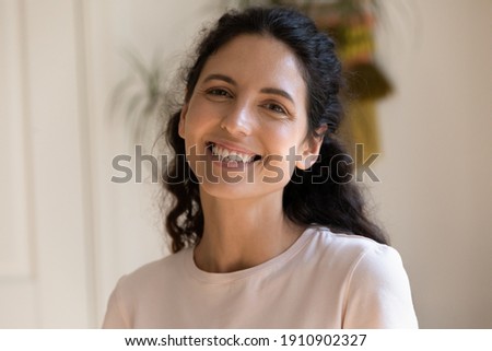Adorable millennial female posing for headshot portrait smiling looking at camera. Profile picture of happy young woman with shiny smile making video call from home taking part in virtual conference