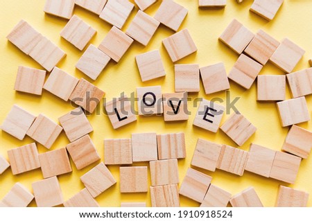 Pile of wooden letters on the surface of a yellow background with spell love, valentine's day. Selective focus.