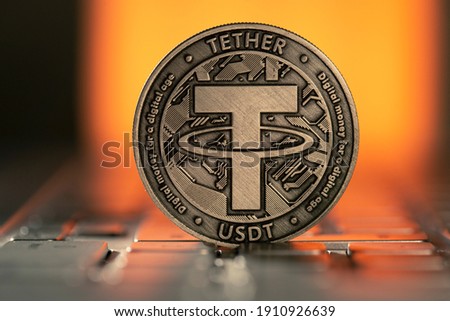 Tether USDT Cryptocurrency physical coin placed on laptop keyboard and lit with orange light from behind. Royalty-Free Stock Photo #1910926639