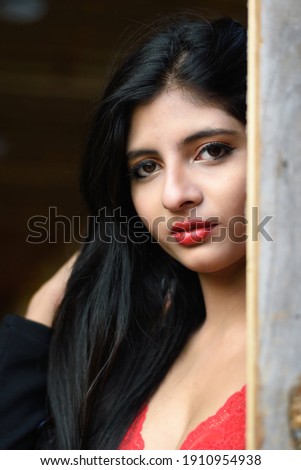 Portrait of very beautiful young attractive Indian woman wearing red outfit with black jacket with half face near a wooden door in a blurred background. Lifestyle and Fashion.