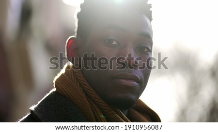 Young black man standing outside wearing coat and scarf looking at camera portrait