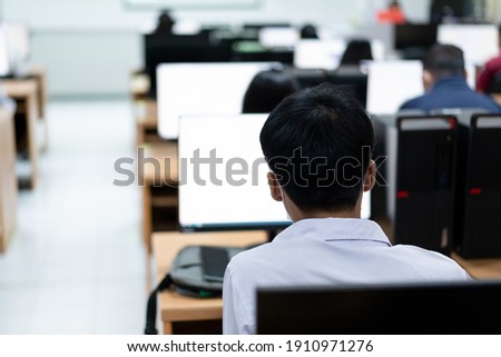 Blur and selective focus of the adult university learners wearing a face mask while concentrating on doing online examination in the computer room. Serious students working on computer at university