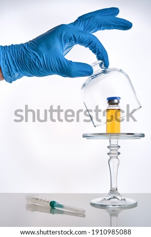 Covid-19 vaccine presentation concept, vial vaccine dose in glass cloche and syringe on mirror surface, white background, selective focus