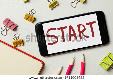 Smartphone with word Start and stationery on white background, flat lay