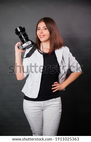 Woman photographer with a SLR camera in her hands posing on a gray background.
