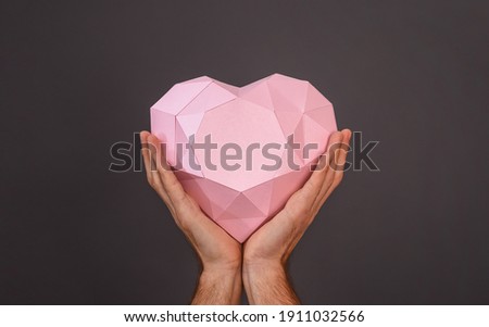 Polygonal heart shape made of paper. Pink heart in a man's hands on a gray background. The concept of Valentine's day and birthday greetings.