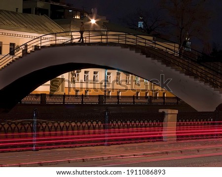 Illuminated embankment with bright light of lamps and a dark sky. Night in the center of Moscow, Russia. Cityscape pedestrian bridge over the river and bright red stripes of traffic lights.