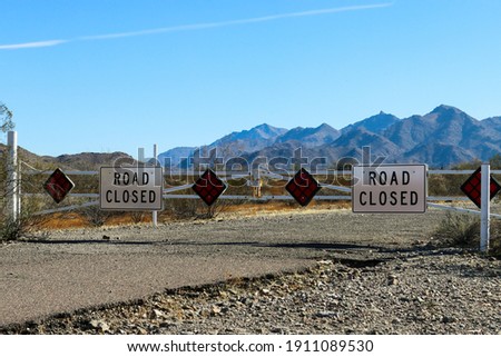 A road closed gate on a road in Avondale, Arizona.  There are mountains in the background.