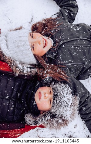 a girl with long hair open eyes and a boy with closed eyes laughs outside it is snowing day in warm clothes and a knitted hat braces on the teeth lying on the back in the snow portrait