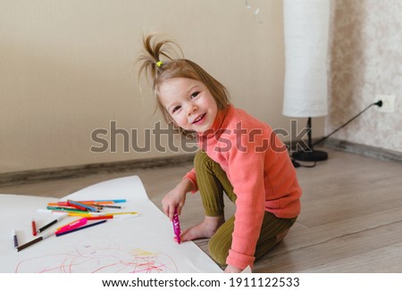A little girl, sitting on the floor, enjoys creativity, drawing pictures with pencils on paper.