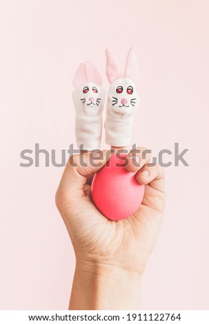 Easter egg in hand with toy bunnies on on fingers.. Minimal holiday concept. 